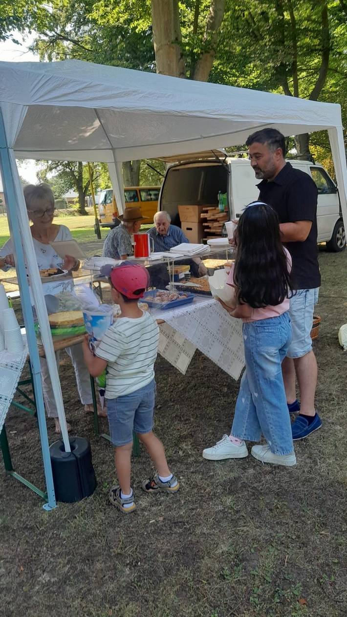 Das Foto zeigt mehrere Personen an einem Kuchenstand.